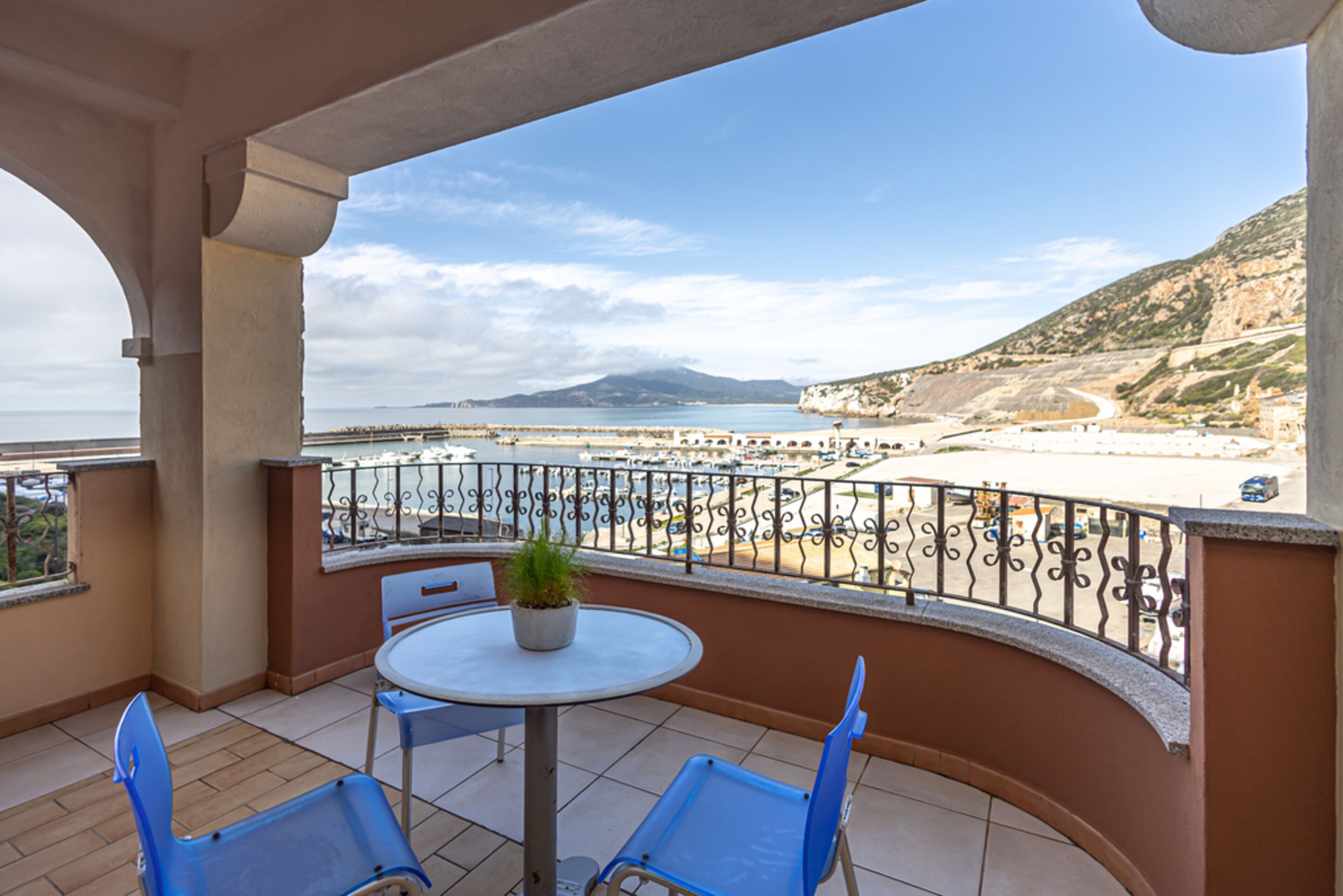 A balcony with a table and chairs, overlooking a beach and mountains.