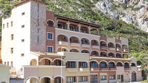 Un hotel de varios pisos con balcones, fachada de piedra y montañas al fondo.