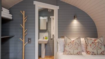 A bedroom with a curved ceiling, a wooden coat rack, a white sink, and floral-patterned pillows.