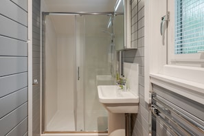 Bathroom features a glass-enclosed shower, a wall-mounted sink, and a mirror above.