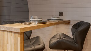 Une cuisine moderne avec un plan de travail en bois, deux fauteuils en cuir et une étagère intégrée où sont rangées des assiettes et des verres.