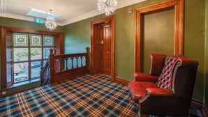 A room with a plaid carpet, a red leather chair, a wooden door, and a chandelier.