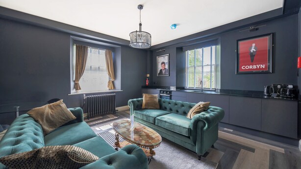 A modern living room with a teal sofa set, a coffee table, and a kitchen area visible in the background.