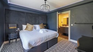 A modern hotel room with a large bed, a bedside table, a lamp, and a bathroom visible through an open door.