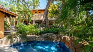 A swimming pool surrounded by tropical vegetation and a building with a tiled roof. - Casa  Don Juan (Compostela)