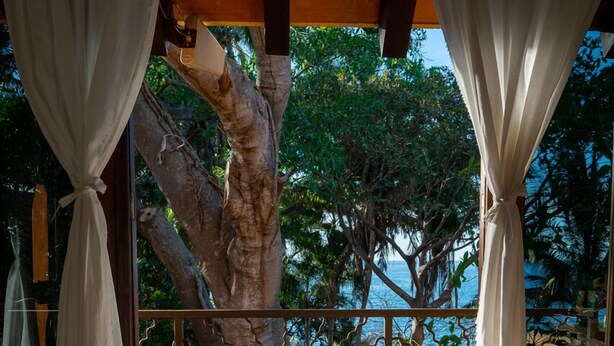 A balcony with white curtains, a tree outside, and a view of the sea. - Casa  Don Juan (Compostela)