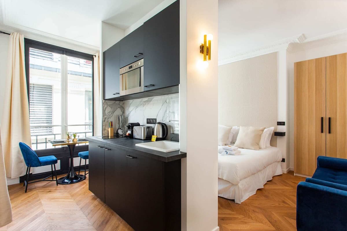 Quarto de hotel moderno com cozinha, mesa de jantar com cadeiras, cama e guarda-roupa.