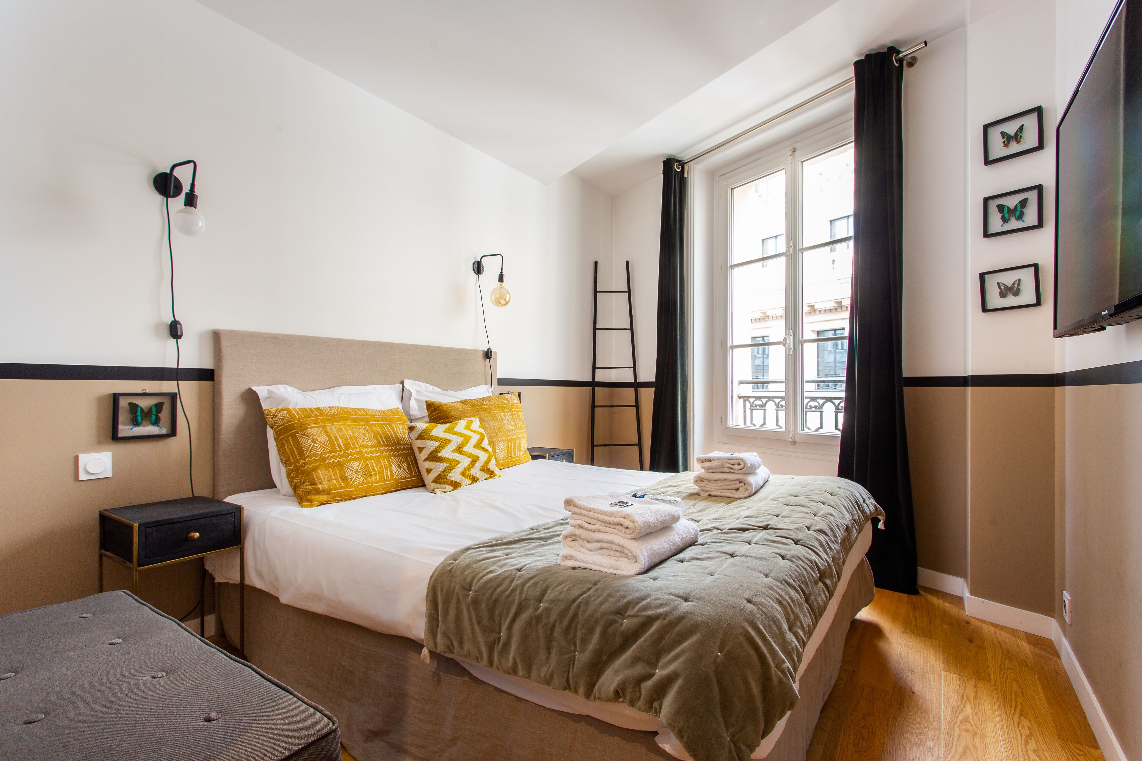 Habitación de hotel ordenada con cama, mesita de noche, lámpara y ventana con cortinas.
