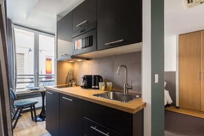 Una cocina compacta con armarios oscuros, un lavamanos de acero inoxidable y una encimera de madera.