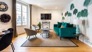 A modern living room with a green sofa, a TV mounted on the wall, and a dining area with chairs and a table. - Résidence Paris Boetie (Paris)