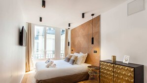 A modern hotel room with a large bed, a wooden headboard, a small side table, and a TV mounted on the wall. - Résidence Paris Boetie (Paris)