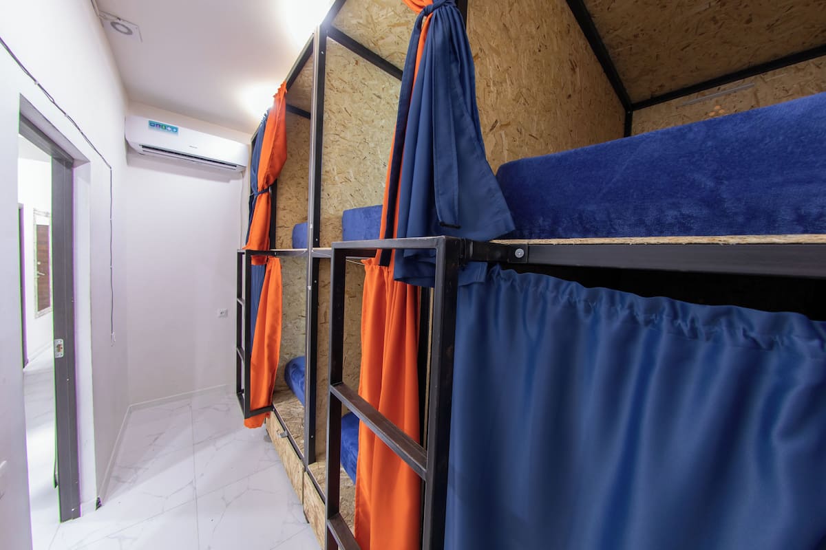 A bunk bed room with blue and orange curtains, a white air conditioning unit, and a wooden ceiling.