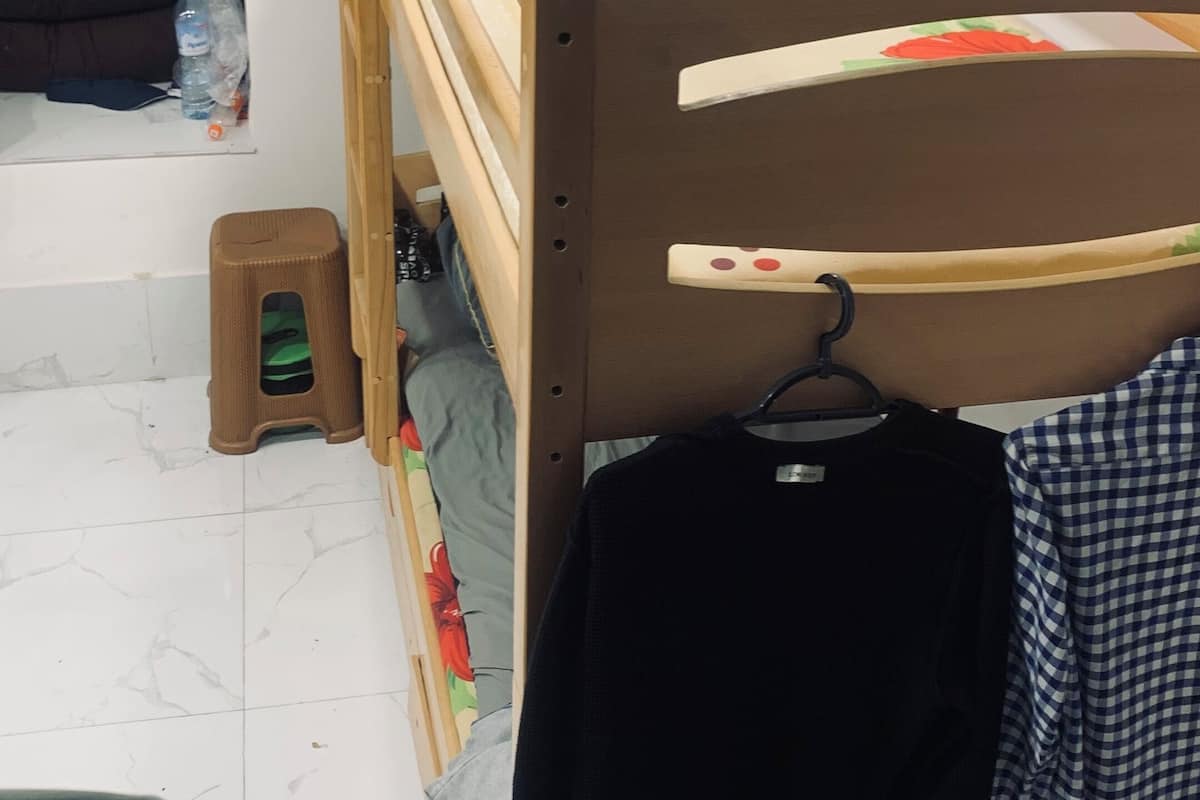 A bunk bed with a wooden frame, a small stool, and a pair of shoes on the floor.
