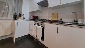 Cozinha moderna com armários brancos, fogão, pia e janela com cortinas leves.