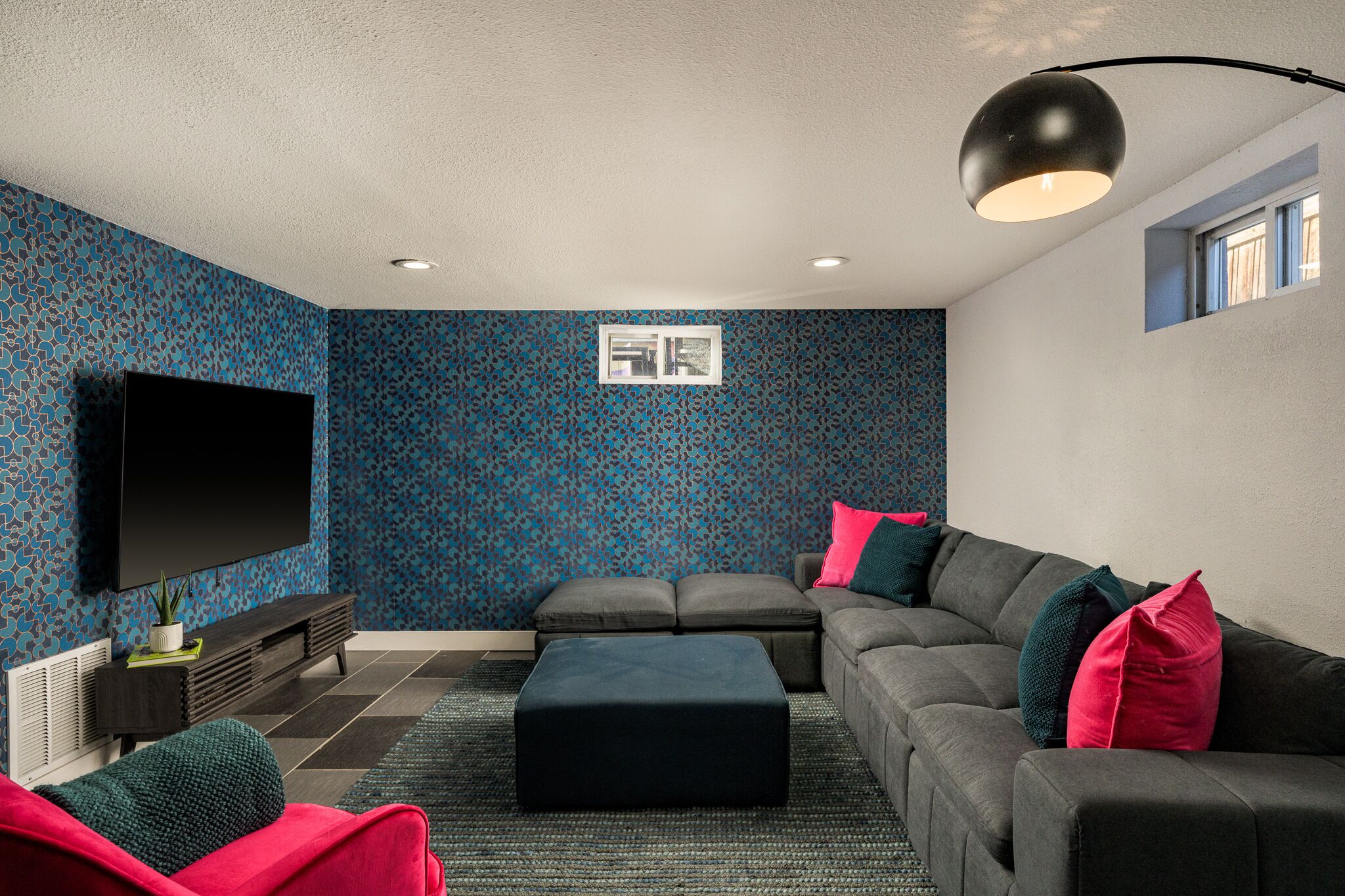 Uma sala de estar moderna com uma televisão de tela plana grande, sofás cinzas e uma parede azul estampada.