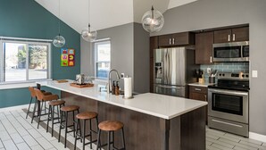 Une cuisine moderne dotée d’un grand îlot central, d’appareils électroménagers en acier inoxydable et de tabourets de bar.