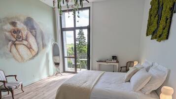 Un dormitorio con un ventanal grande, una cama con ropa de cama blanca, una lámpara colgante de plantas y un mural en la pared.