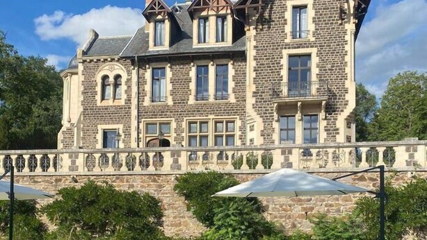 Un edificio grande de piedra con piscina y tumbonas.