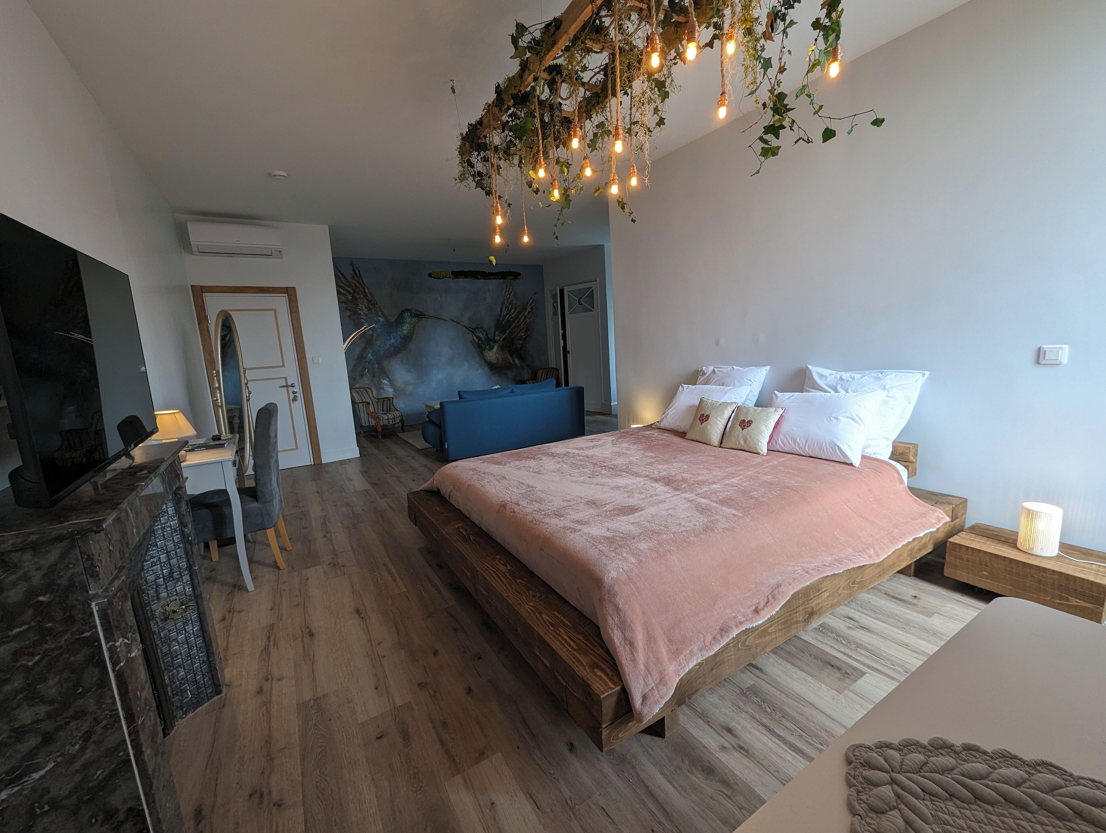 Une chambre avec un lit en bois, un canapé bleu, un bureau avec une chaise et une fresque murale.