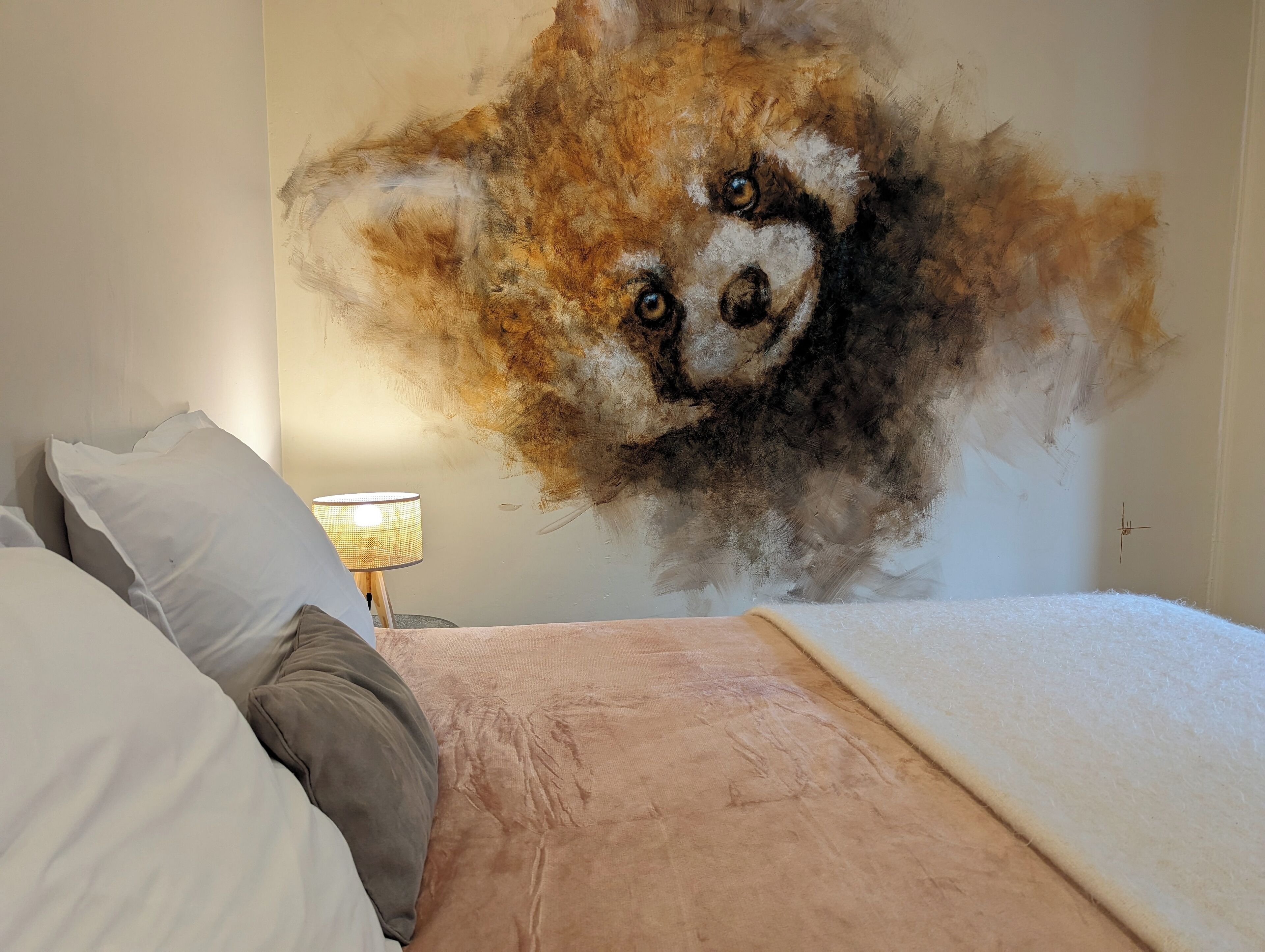 Un dormitorio con un cuadro grande de un zorro en la pared, una cama con almohadas y una lámpara de noche.