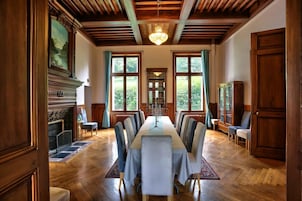 Un comedor formal con una larga mesa, sillas, una chimenea, estanterías y ventanas grandes.