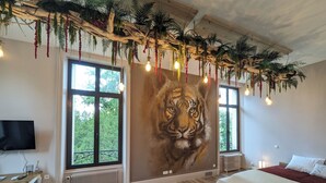 Un dormitorio con un ventanal grande, una cama, un televisor y un mural de un tigre.