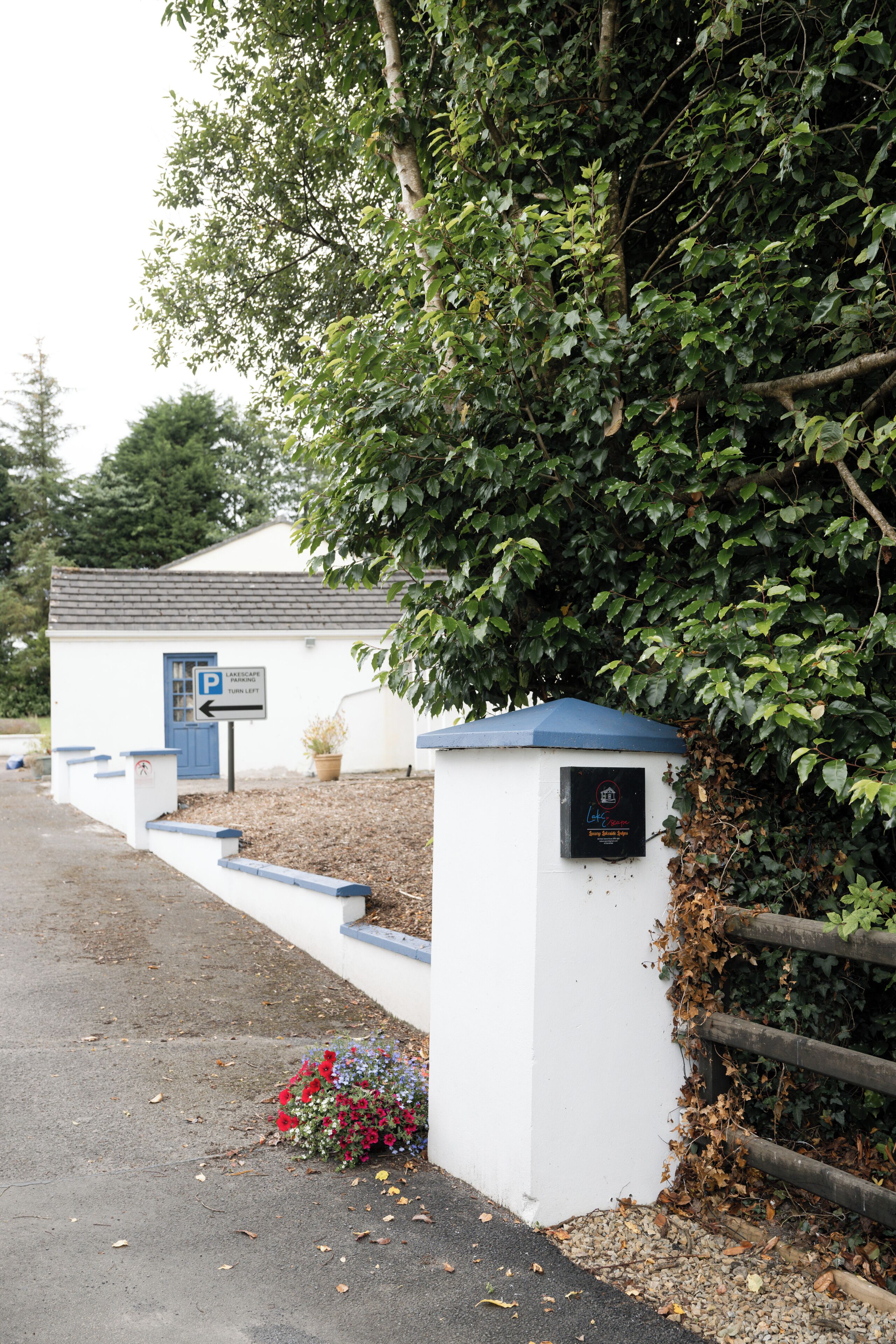 Ein weißes Gebäude mit blauem Dach, einem Parkplatzschild und einem Blumenbeet mit roten Blüten.