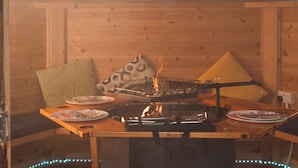 Interior de madeira com uma mesa posta para refeições, incluindo uma churrasqueira e pratos.
