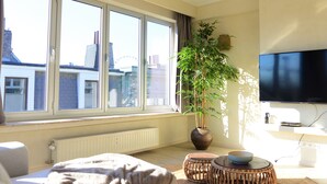 Una sala de estar moderna con un ventanal grande, una planta en maceta, un televisor de pantalla plana y una zona de estar confortable.