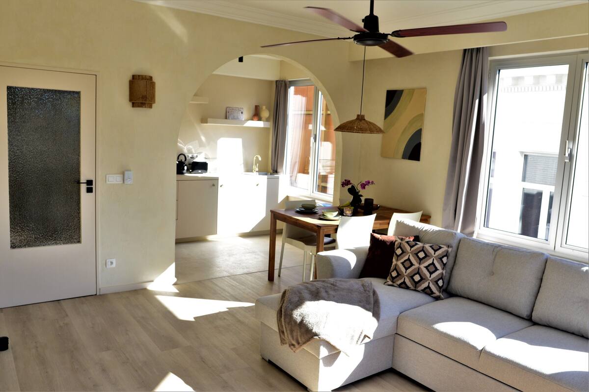 Ein modernes Wohnzimmer mit einer Couch, einem Esstisch und einer Küche im Hintergrund.