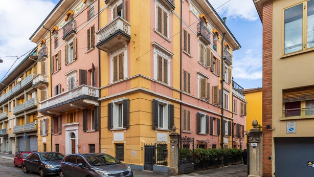 A multi-story building with balconies, a gated entrance, and parked cars on the street. - Comfort Urbano a Porta Maggiore by Wonderful Italy (Bologna)