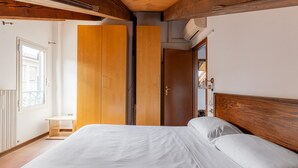 A bedroom with a wooden headboard, a bed with white bedding, a wooden wardrobe, and a small wooden table. - Comfort Urbano a Porta Maggiore by Wonderful Italy (Bologna)