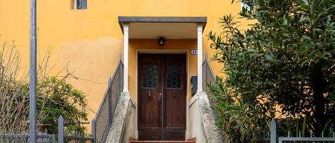 A building with a yellow facade, a wooden door, and a staircase leading to the entrance.