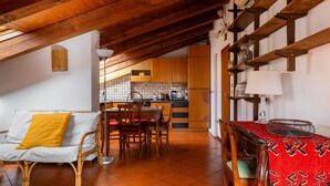 A cozy kitchen with wooden beams, a dining area with a table and chairs, and a sofa with a yellow cushion. - Comfort Urbano a Porta Maggiore by Wonderful Italy (Bologna)