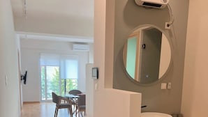 En moderne lejlighed med trægulv, spiseplads med stole, et rundt spejl og en indbygget vask.