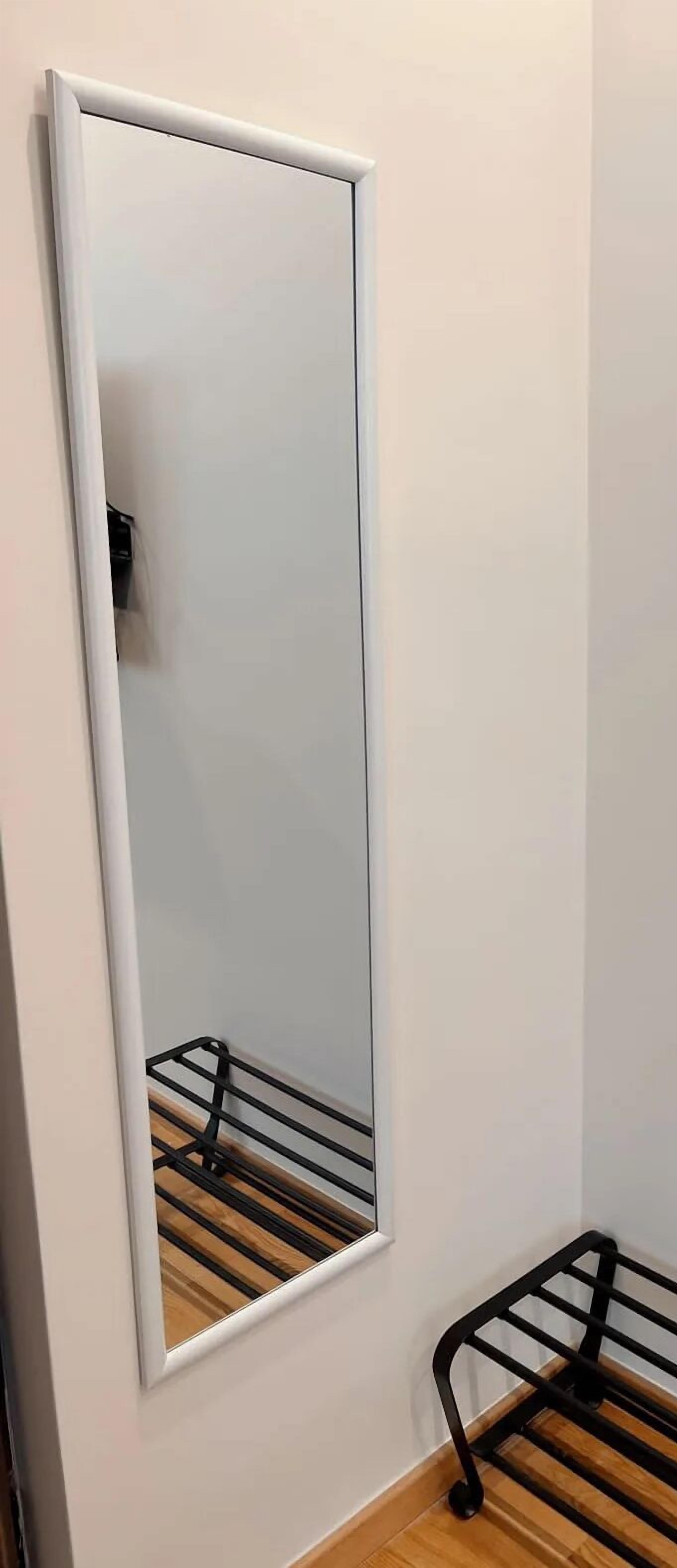 Huoneessa on suuri peili seinällä, musta metallihylly ja puulattia.