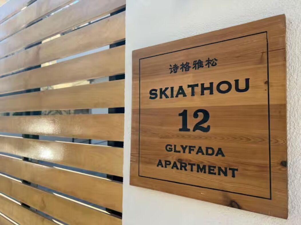 Un letrero de madera con el texto 'SKIATHOU 12 GLYFADA APARTMENT' que indica el nombre y número del apartamento.