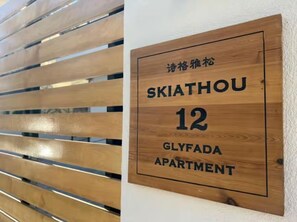 A wooden sign with the text "SKIATHOU 12 GLYFADA APARTMENT" indicating the name and number of the apartment. - Skiathou 12 Glyfada Residences (Glyfada)