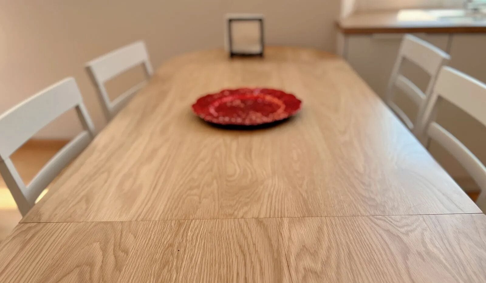 A wooden dining table with a red placemat in the center, surrounded by white chairs.