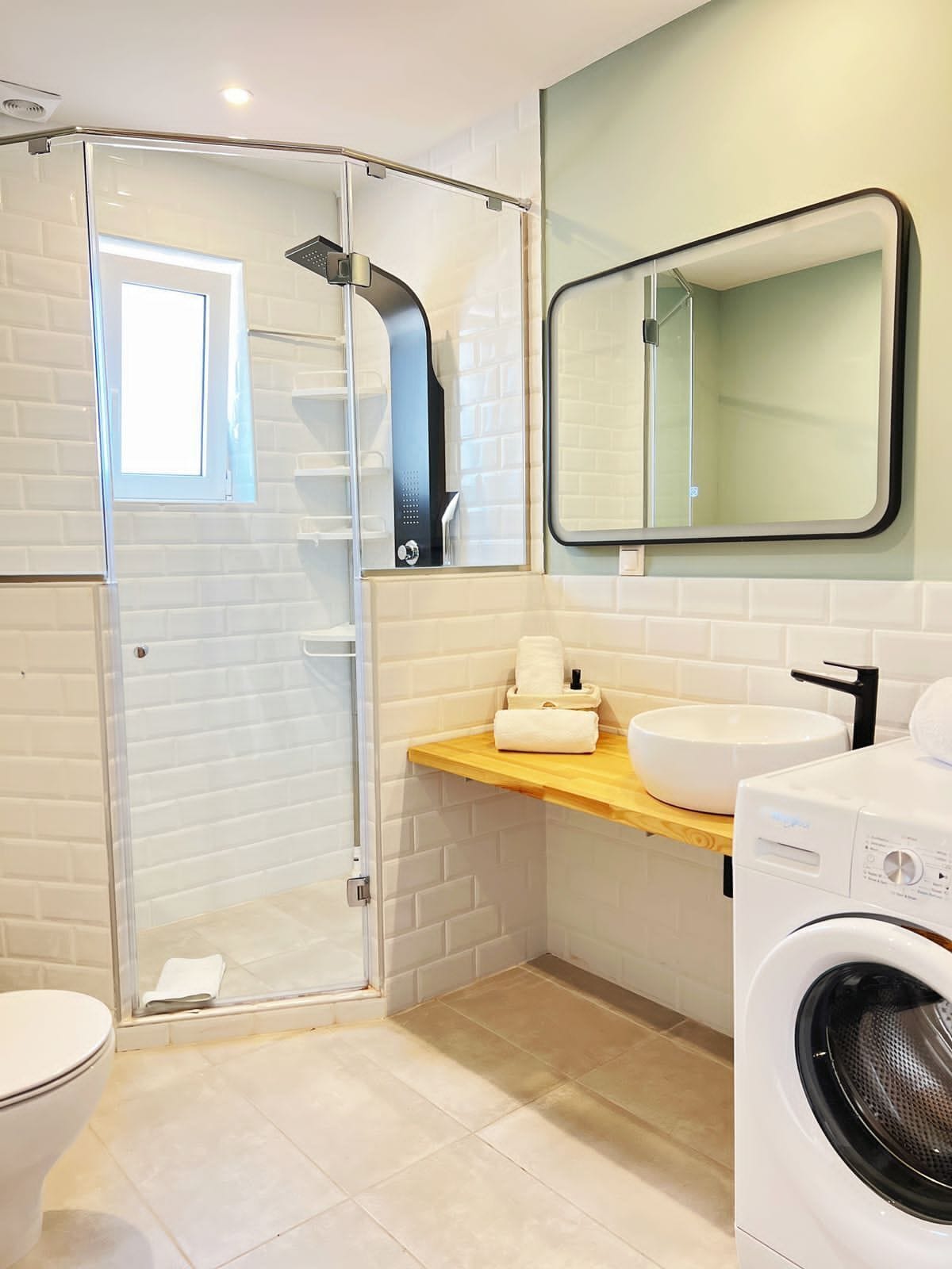 Une salle de bain moderne avec une douche à parois de verre, un lavabo blanc, un miroir et un lave-linge.