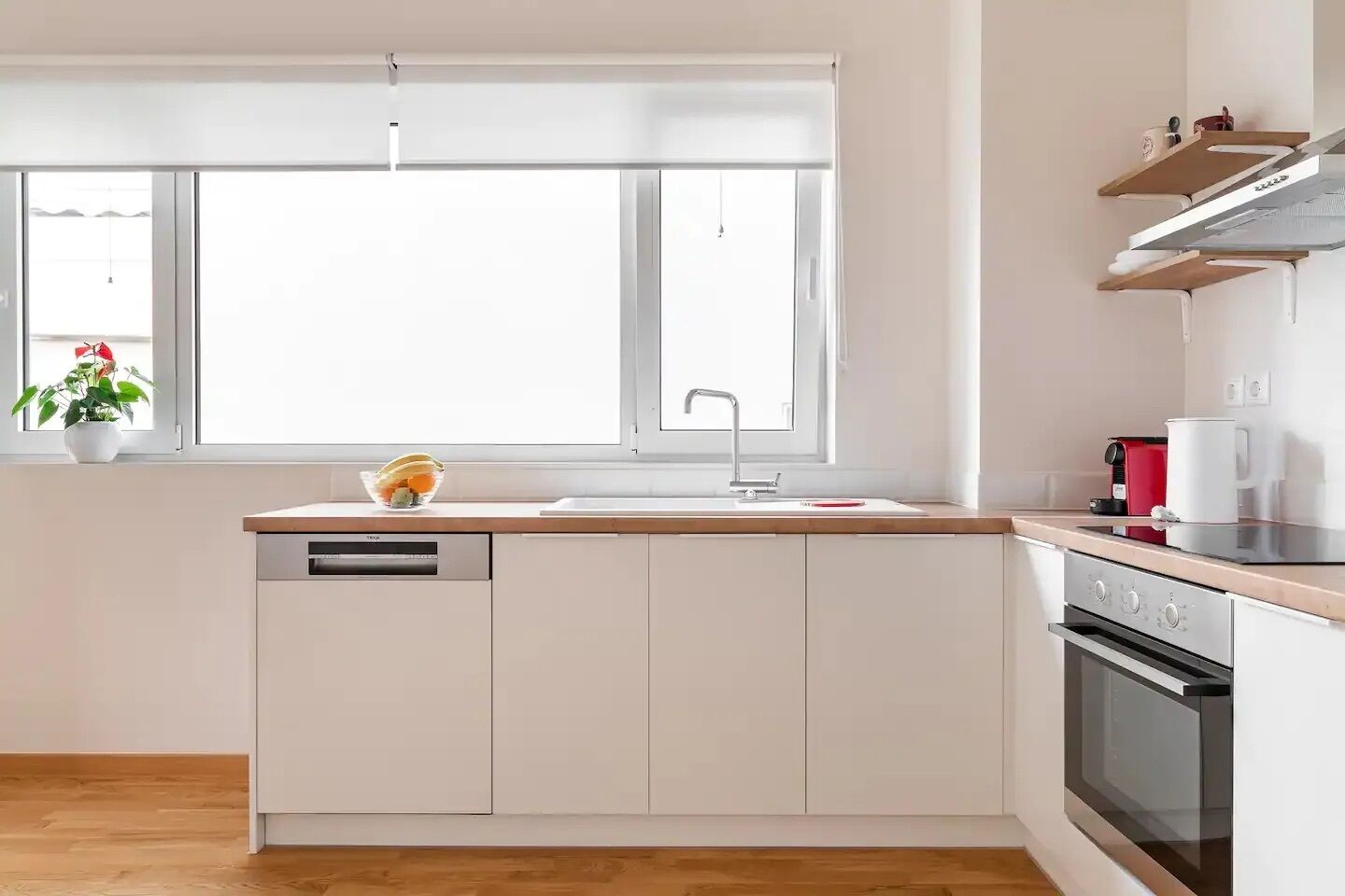 A modern kitchen with a dishwasher, sink, and oven. There is a window with a view of the outdoors.