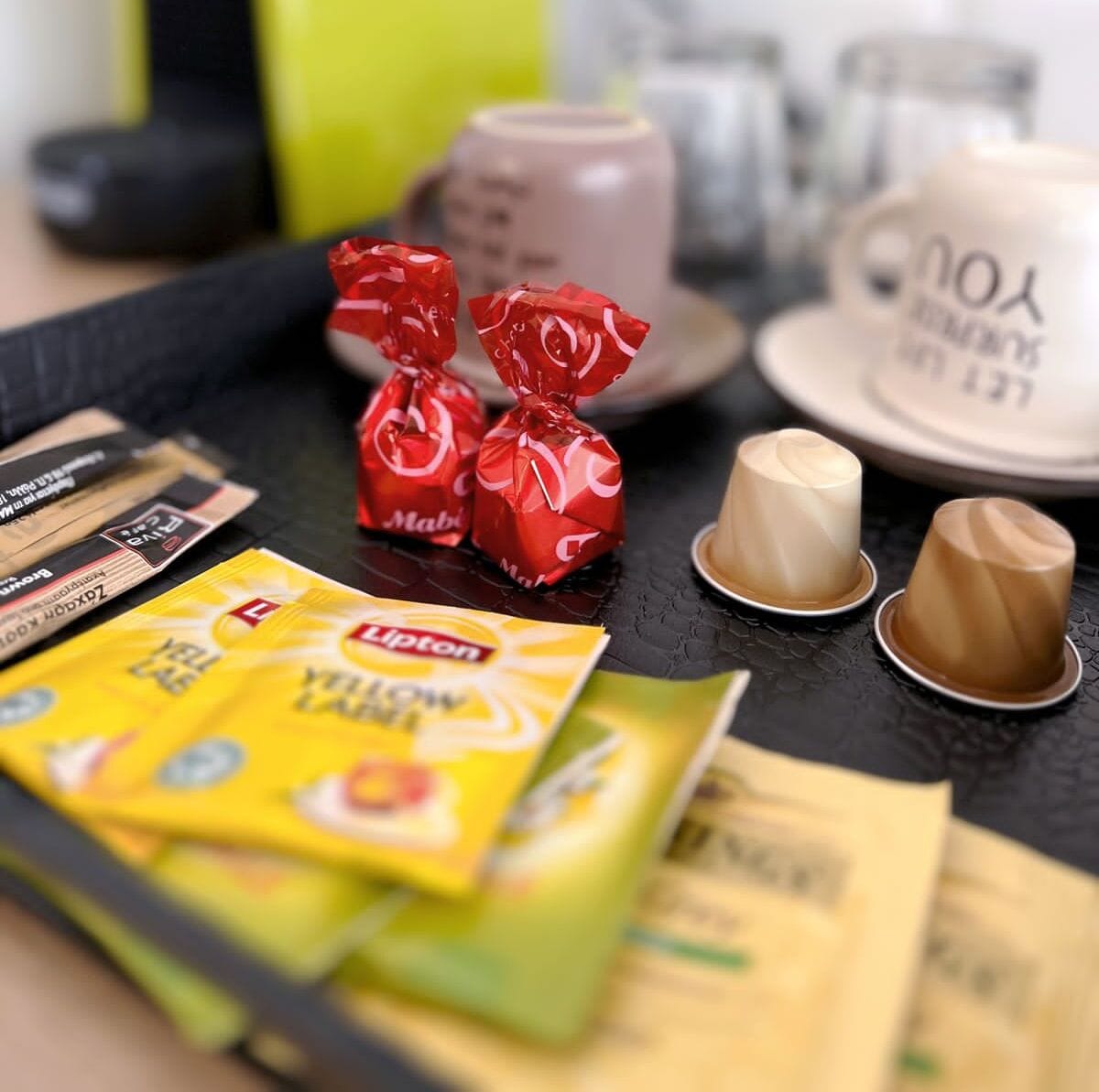 Un plateau contenant divers aliments, notamment des bonbons emballés, une tasse de café et des sachets de thé Lipton.
