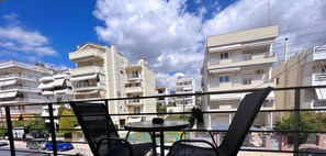 A balcony with two chairs and a table, overlooking a residential area with multi-story buildings. - Skiathou 12 Glyfada Residences (Glyfada)