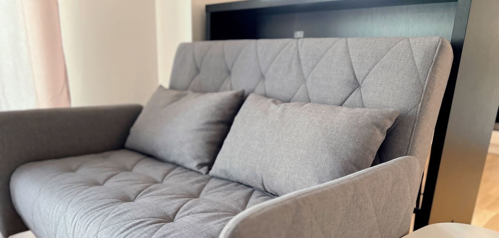 A grey upholstered armchair with a quilted backrest and two cushions.