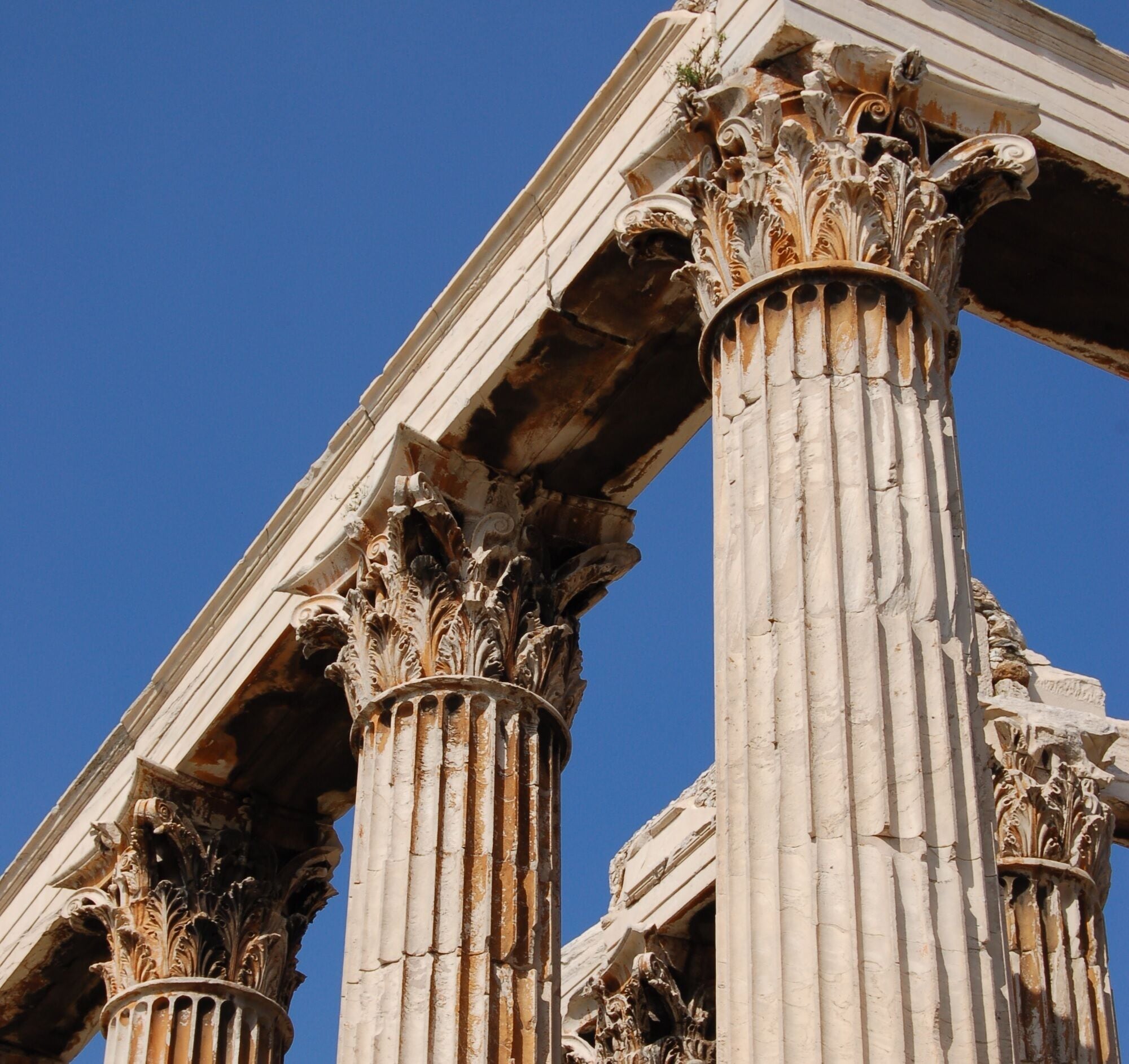 Ancient Greek columns with intricate carvings and a clear blue sky in the background.