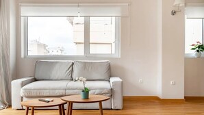 En moderne stue med en grå sofa, to træsofaborde og et stort vindue, der giver naturligt lys.
