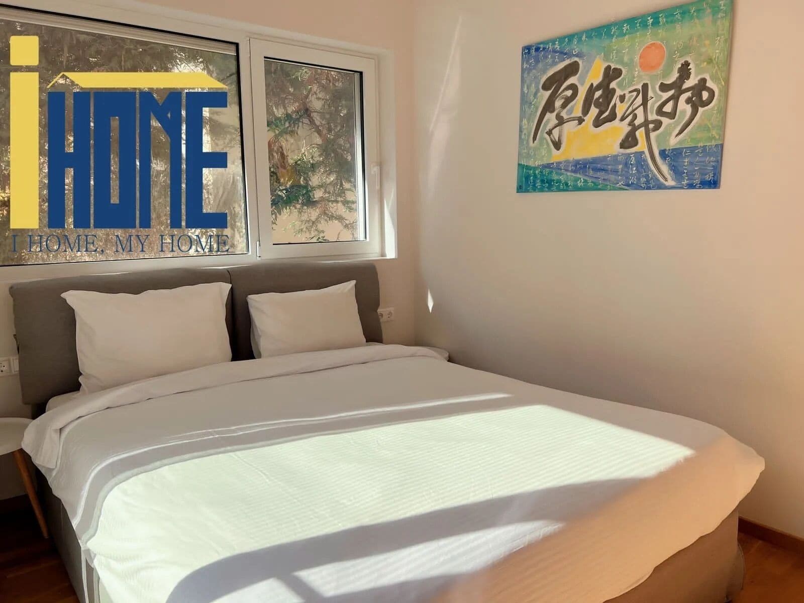 A bedroom with a bed, a window with a view of trees, and a wall with a painting.