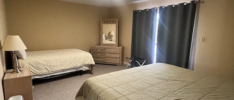 A hotel room with two beds, a dresser, a mirror, a lamp, and a window with curtains.