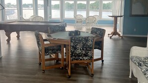 A spacious room with a pool table, a round dining table with chairs, and large windows offering a view of a body of water. - The Moorings Hotel and Marina  (Carrabelle)
