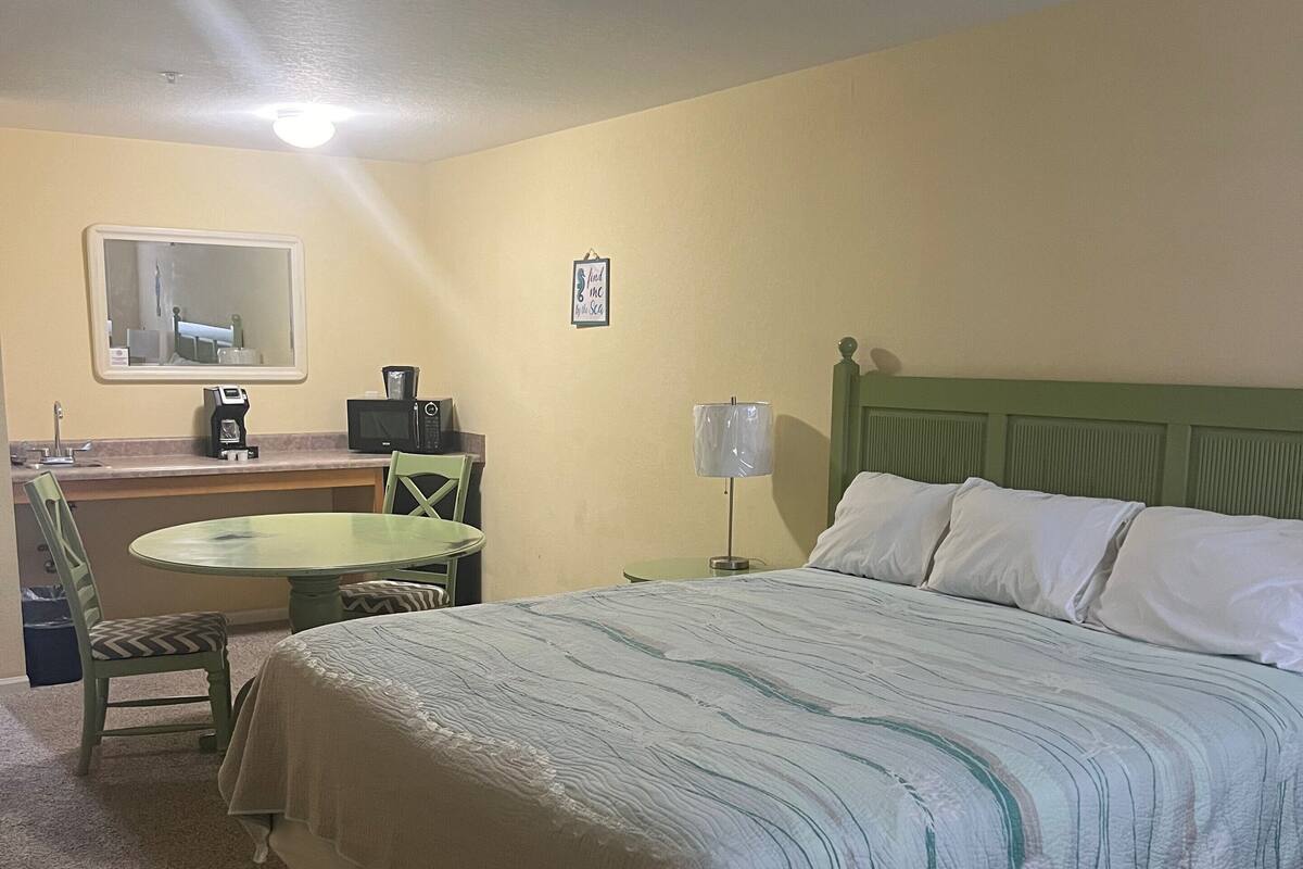 Ein Hotelzimmer mit einem Bett, einem Schreibtisch mit Stuhl, einer Lampe und einem kleinen Tisch.